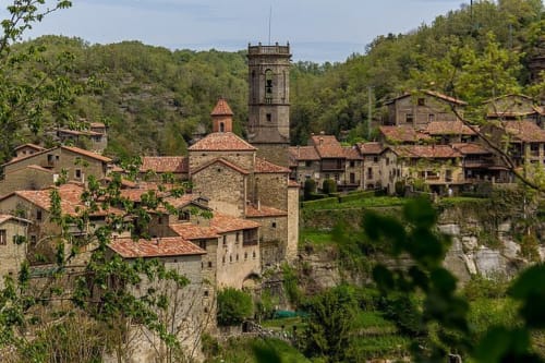 Villaggio medievale di Vallgorguina vicino Barcellona con edifici in pietra e campanile immerso tra colline verdeggianti e alberi