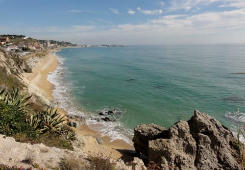 Vista della spiaggia costiera con acque turchesi, sabbia dorata e edifici su scogliera vicino a Vallgorguina, Barcellona
