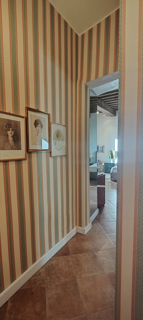 Ingresso a corridoio a righe della Suite Patrimonio dell'Umanità ad Assisi con ritratti incorniciati e porta aperta verso la camera da letto