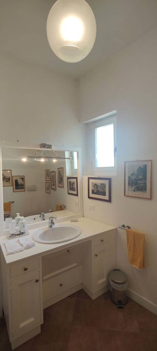 Bagno luminoso nella World Heritage Suite di Assisi con mobile bianco, specchio, lucernario ovale, quadri incorniciati e accessori moderni