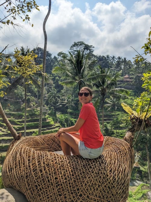 Femme assise sur une structure de panier tressé surplombant une vallée tropicale luxuriante avec palmiers
