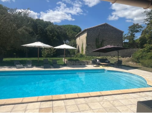 La piscine de La Conciergerie De Franck avec bâtisse en pierre, transats, parasols et jardins soignés à Boissières,