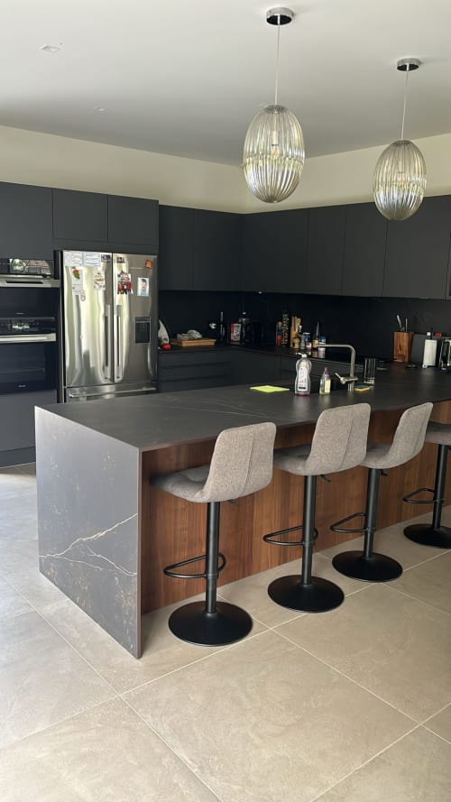 Modern kitchen with dark cabinetry, marble island, bar seating, and pendant lighting at La Conciergerie De Franck villa in