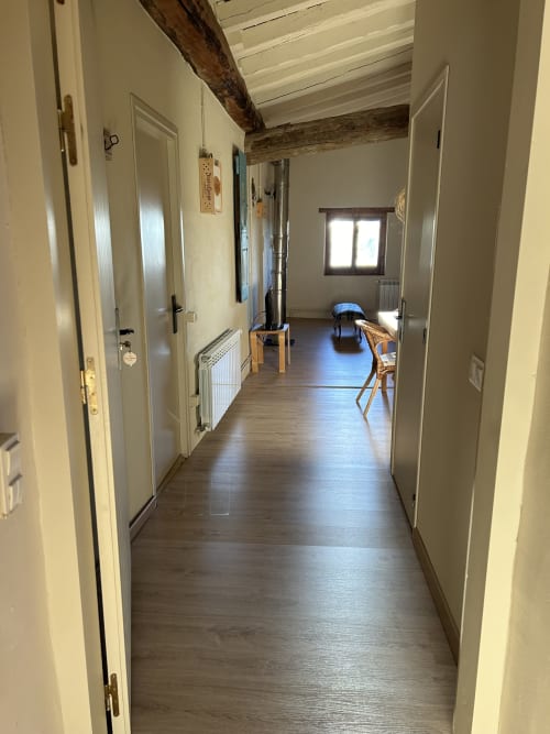Pasillo luminoso de la casa rural Casa Tapiolas con vigas de madera vista, puertas blancas y suelo de madera oscura en Molló