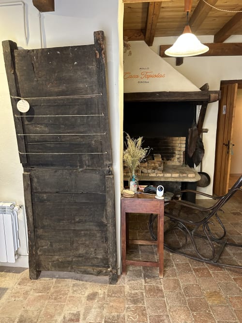 Chimenea rústica con puerta de madera oscura en la casa rural Casa Tapiolas en Molló, Girona, vigas expuestas y estilo tradicional
