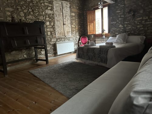 Dormitorio rústico de piedra en Casa Tapiolas en Molló con cama de madera, zona de estar y vistas a la montaña