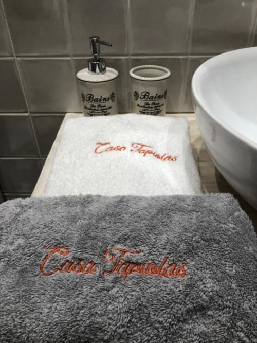Equipamiento de baño Casa Tapiolas: toallas bordadas, dosificadores de jabón y bañera blanca en Molló, Girona