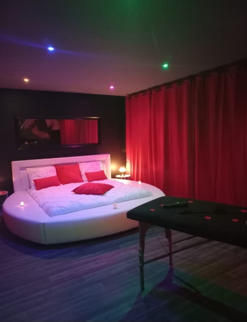 Chambre moderne avec lit rond blanc, coussins rouges, éclairage LED ambiant et billard à La Maison du Plaisir