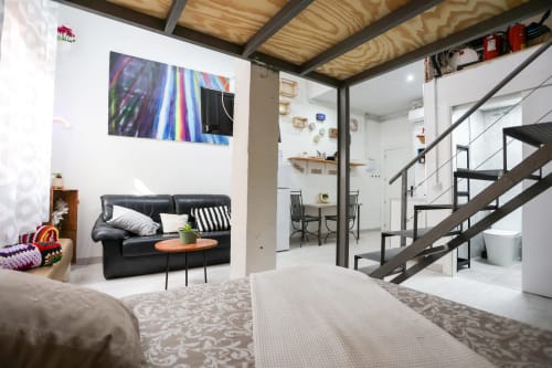 Moderno loft en Apartamentos Huelintown, Málaga con sofá de cuero negro, obras de arte coloridas y escalera de metal