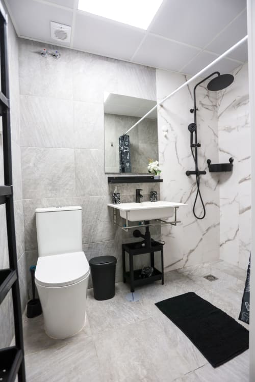 Baño moderno en Apartamentos Huelintown, Málaga con azulejos de mármol, accesorios negros, ducha de lluvia y lavabo elegante