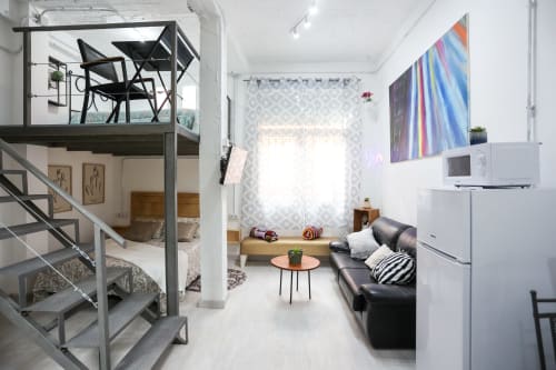 Apartamento moderno en Apartamentos Huelintown, Málaga, con dormitorio loft, sofá negro y arte mural colorido