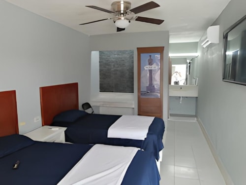 Habitación doble Hotel Estrella Matamoros con camas gemelas, cabeceros rojos, ventilador de techo y baño moderno al fondo