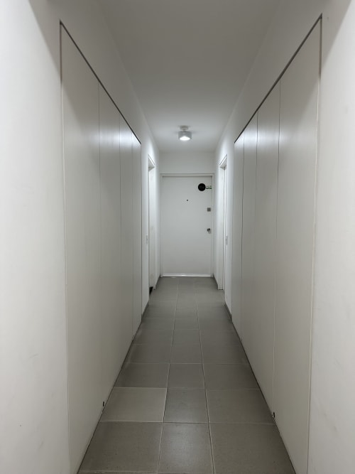 Moderno pasillo del departamento Pares Homes en la Ciudad de México con paredes blancas, piso de azulejos grises y puertas cerradas