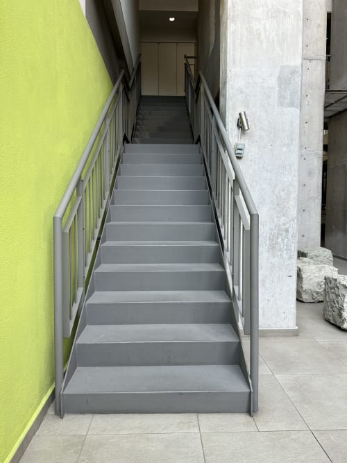 Escalera gris con barandales metálicos en departamento moderno de CDMX en Pares Homes, pared amarilla visible