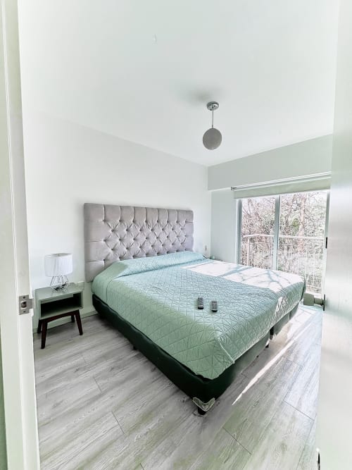 Moderna habitación en apartamento Pares Homes en CDMX con cama queen, cabecera gris y ventanales del piso al techo