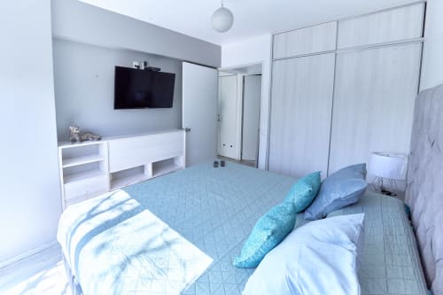 Recámara moderna en departamento Pares Homes en Ciudad de México con ropa de cama azul, TV de pared y abundante luz natural