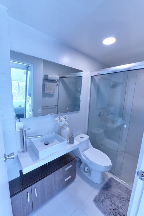 Baño moderno en apartamento Pares Homes CDMX con lavabo tipo recipiente, vanidor oscuro, ducha lluvia y muros con azulejos blancos.