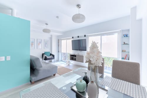 Sala de estar de apartamento moderno en Ciudad de México con pared de acento turquesa, asientos grises y ventanales del piso al techo en Pares
