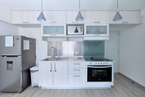 Cocina blanca moderna en apartamento de Pares Homes, Ciudad de México, con electrodomésticos de acero inoxidable e iluminación colgante