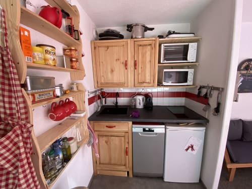 "Cuisine de l'appartement 319 à Vars-les-Claux, alliant des touches de rouge et de bois naturel, offrant un espace moderne et chaleureux, entièrement équipée pour préparer des repas conviviaux après une journée de ski."