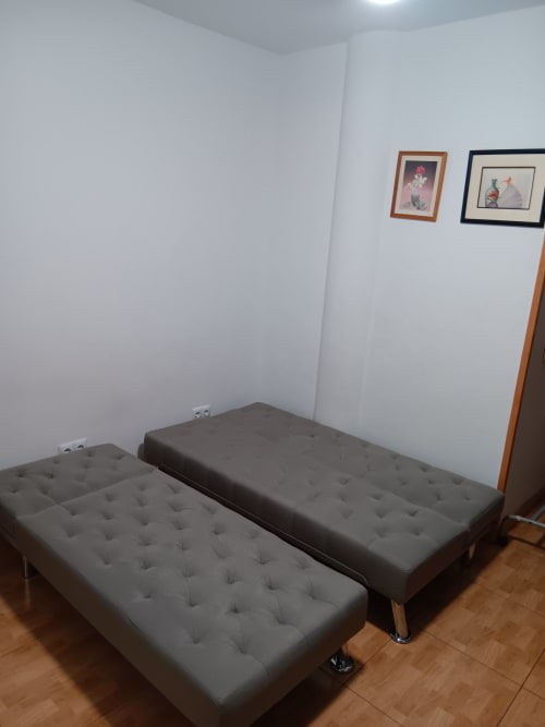 Two gray upholstered beds in Casa Ferrer Barcelona apartment bedroom with white walls and framed artwork