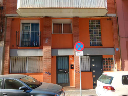 Brick facade of Casa Ferrer Barcelona apartment in L'Hospitalet de Llobregat with orange exterior, windows, and no parking