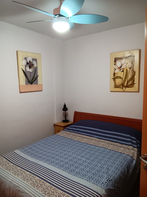 Modern bedroom at Casa Ferrer Barcelona with wooden bed, blue striped bedding, ceiling fan, and floral artwork on white