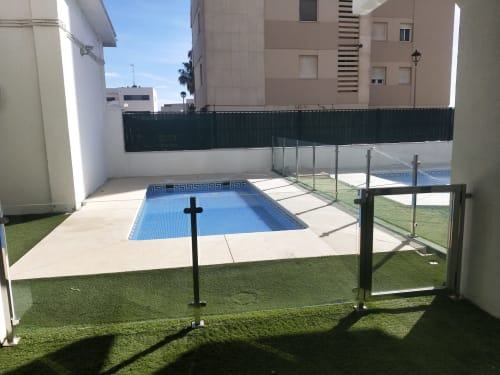 Zona de piscina del apartamento en Wehost Costaluz, Puerto Santa María, con piscina olímpica azul, jardines verdes y residencias adyacentes