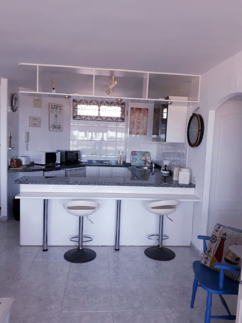 Cocina moderna blanca con isla central, encimeras de granito oscuro y ventanales con vistas al mar en apartamento de Puerto Santa María