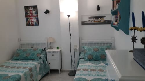 Moderna habitación de apartamento con camas gemelas, ropa de cama turquesa, mesita blanca, lámpara de pie y arte decorativo en la pared en Puerto