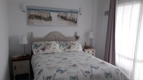 Dormitorio costero luminoso con ropa de cama estampada de mariposas, obra de arte marina, mesitas de noche con lámparas y acceso a balcón en Puerto
