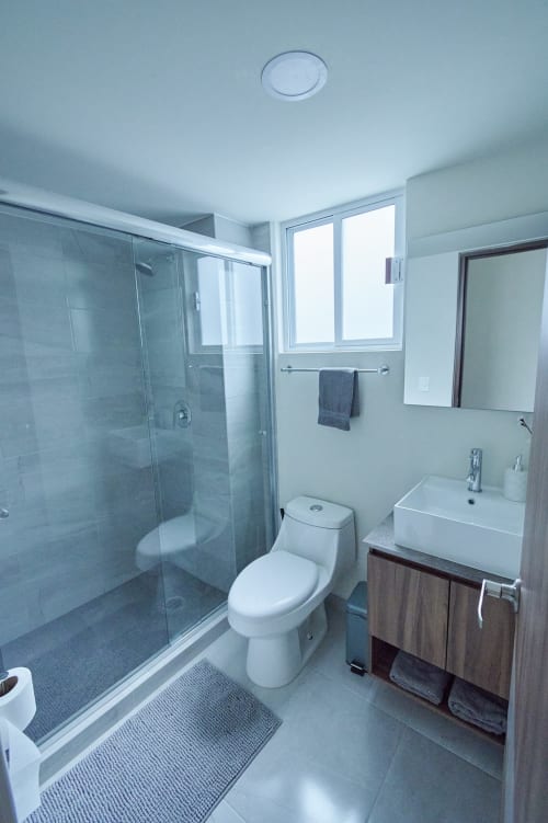 Baño moderno en departamento Pares Homes de la Ciudad de México con ducha de vidrio, lavabo blanco, inodoro y piso de azulejos azules