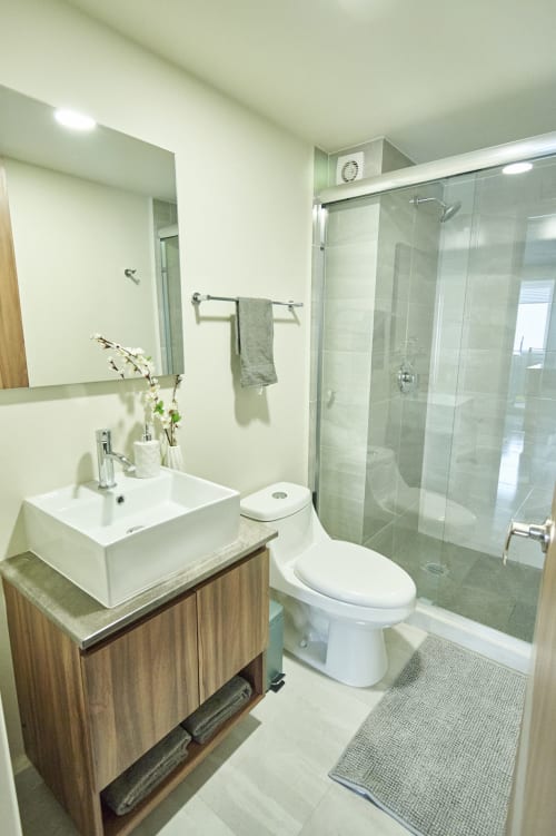 Baño moderno en apartamento de Pares Homes CDMX con lavabo de cerámica, ducha con cabina de vidrio y acabados en azulejos blancos