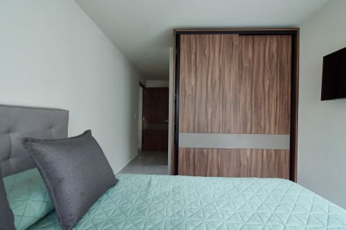 Habitación moderna en apartamento Pares Homes CDMX con ropa de cama menta, cabecera gris y armario de madera