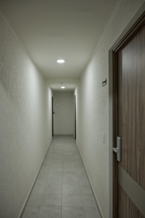 Pasillo moderno del departamento Pares Homes en CDMX con paredes blancas, iluminación empotrada y puerta efecto madera