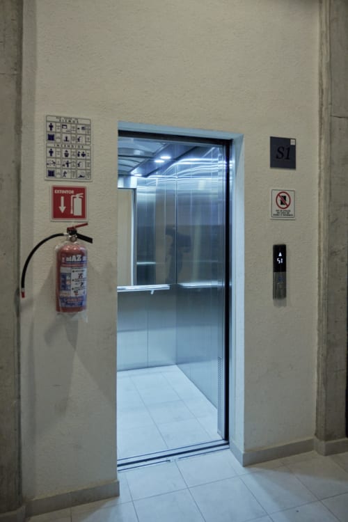 Entrada moderna del ascensor en apartamento Pares Homes en Ciudad de México con señalización de seguridad y extintor