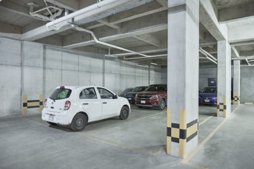 Garaje de estacionamiento subterráneo en apartamento Pares Homes en CDMX con auto blanco, columnas de concreto y marcas de seguridad amarillas