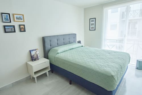 Recámara moderna en departamento Pares Homes, CDMX con cama queen, cabecera gris, mesita blanca y cuadros decorativos.