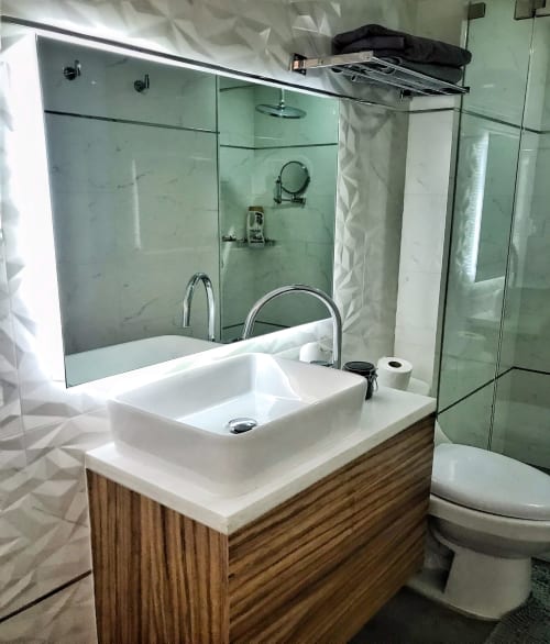 Baño moderno en departamento Pares Homes CDMX con lavabo tipo recipiente, ducha de cristal, inodoro y espejo iluminado