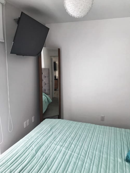 Moderno dormitorio en apartamento Pares Homes en CDMX con ropa de cama menta, TV montada en pared y espejo de cuerpo entero
