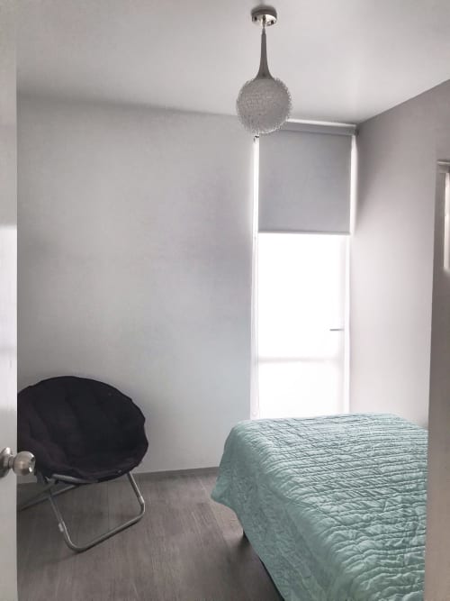 Dormitorio minimalista en apartamento Pares Homes CDMX con cama, silla negra, lámpara colgante y ventana luminosa