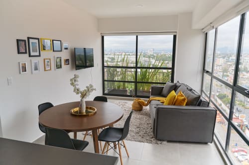 Apartamento moderno en la Ciudad de México con vistas de la ciudad, mesa de comedor, sofá gris con cojines amarillos y ventanales del piso al techo