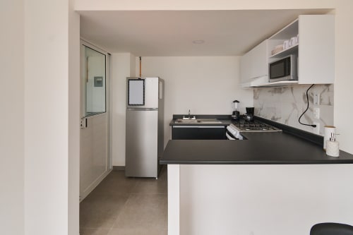 Cocina moderna en apartamento de la Ciudad de México en Pares Homes con encimeras negras, electrodomésticos de acero inoxidable y blanco