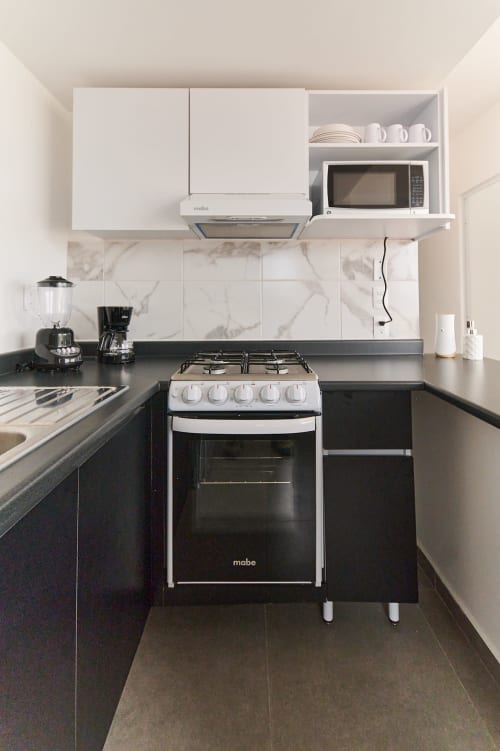 Moderna cocina compacta con electrodomésticos en blanco y negro en el departamento Pares Homes de la Ciudad de México
