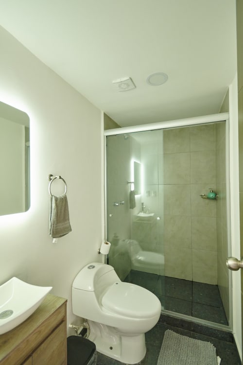 Baño moderno en apartamento de Ciudad de México en Pares Homes con ducha de cristal, inodoro blanco y espejo iluminado