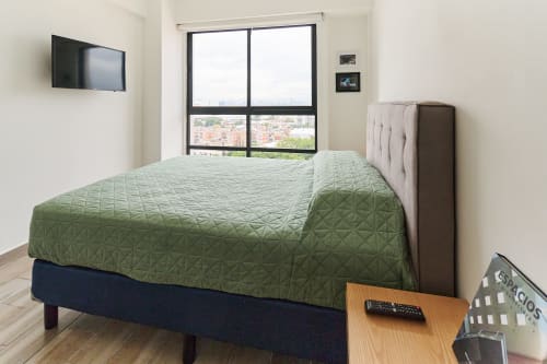 Moderno dormitorio en apartamento de Pares Homes Ciudad de México con cama acolchada verde, televisor de pantalla plana y vistas a la ciudad