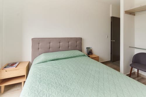 Dormitorio moderno en apartamento Pares Homes CDMX con ropa de cama acolchada verde menta, cabecero capitoné gris y mesitas de madera