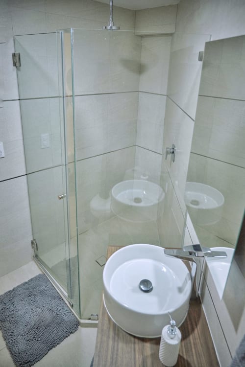 Baño moderno en Pares Homes Ciudad de México con ducha de cristal, lavabo de cerámica blanca y muros revestidos