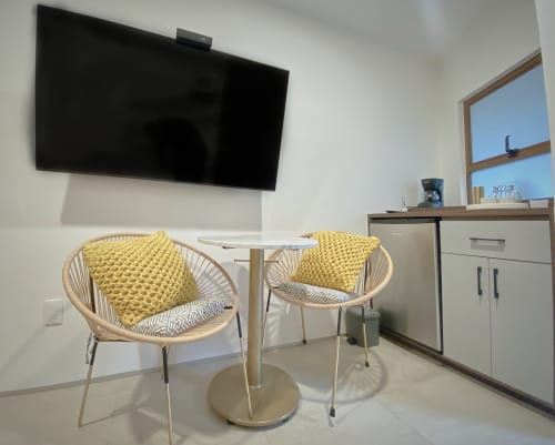 Moderna habitación de hotel en Pares Homes CDMX con dos sillas tejidas, TV montada en pared, escritorio y amplio ventanal con vista a la ciudad.