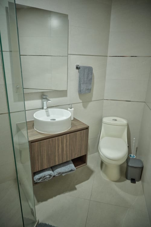 Baño moderno en Pares Homes CDMX con lavabo redondo blanco, mueble de madera, inodoro y paredes revestidas de azulejos grises